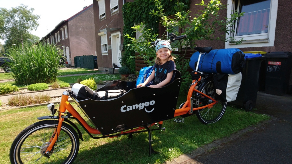 Kind im Lastenfahrrad mit Campingausrüstung